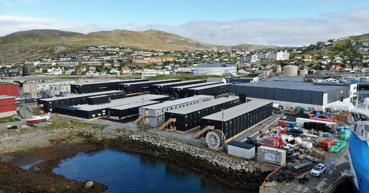 Flygbild över ett tillfälligt personalboende vid vattnet i Hammerfest, med modulbyggnader, hamnområde och omgivande berg i bakgrunden.