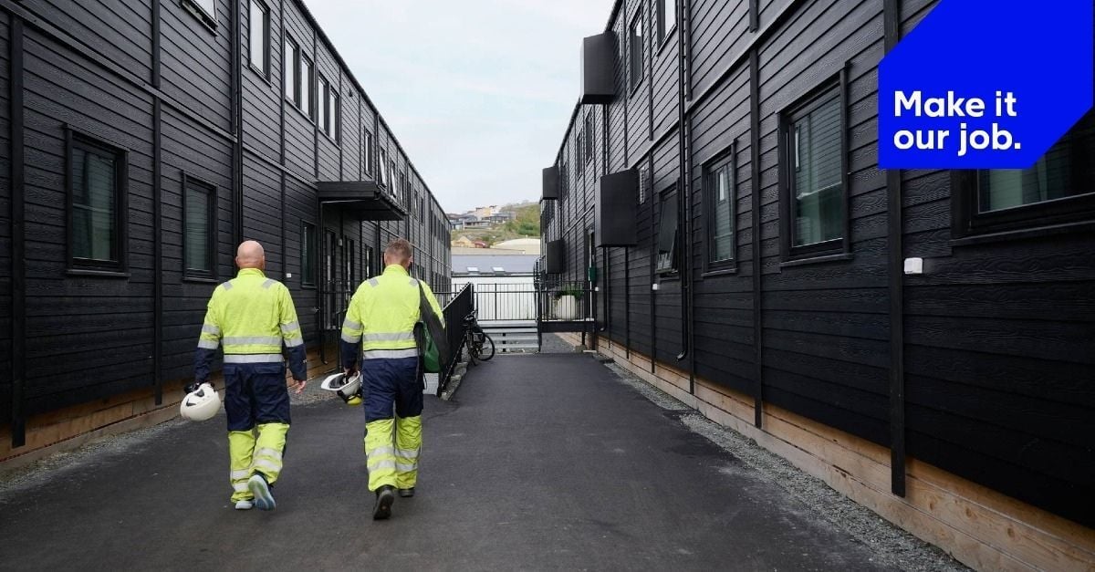 En bild från Adapteo som visar två arbetare i varselkläder som går mellan svarta modulbyggnader för boende, med sloganen ”Make it our job.”